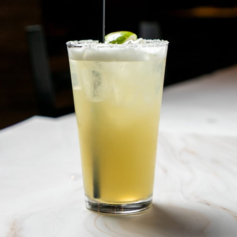 A refreshing margarita with a salted rim and lime wedge, served in a tall glass on a white marble table.